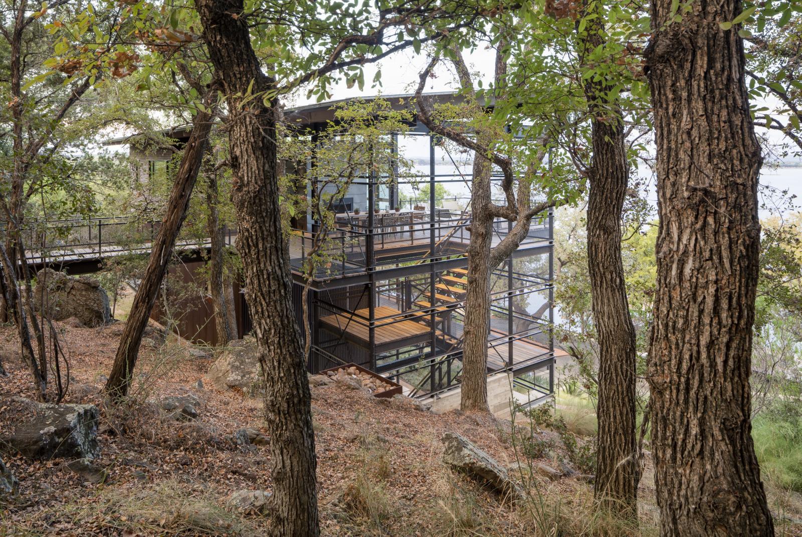 Viewing vertical home from the hillside behind Responding initially to the site’s steeply rising topography, a vertically structured house reveals itself as the obvious design for this lake house. The long, narrow three-story residence dramatically culminates at the top floor