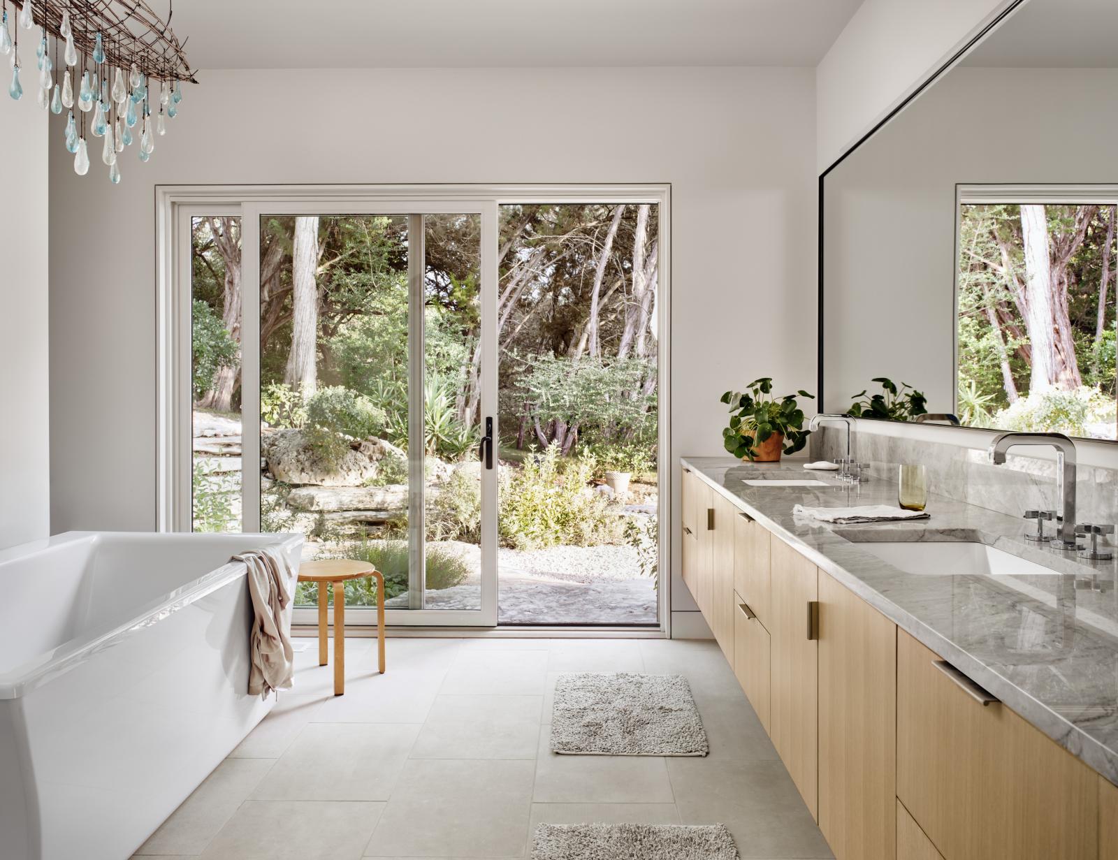 Interior master bathroom connects through a sliding glass door to outdoor landscape 