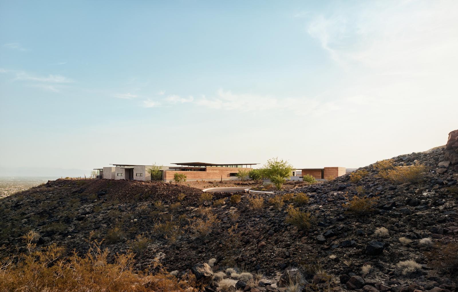 Context view of entire home with views beyond to the city and desert Horizon House uses rammed earth as the primary material which is designed to reflect the surrounding natural topography