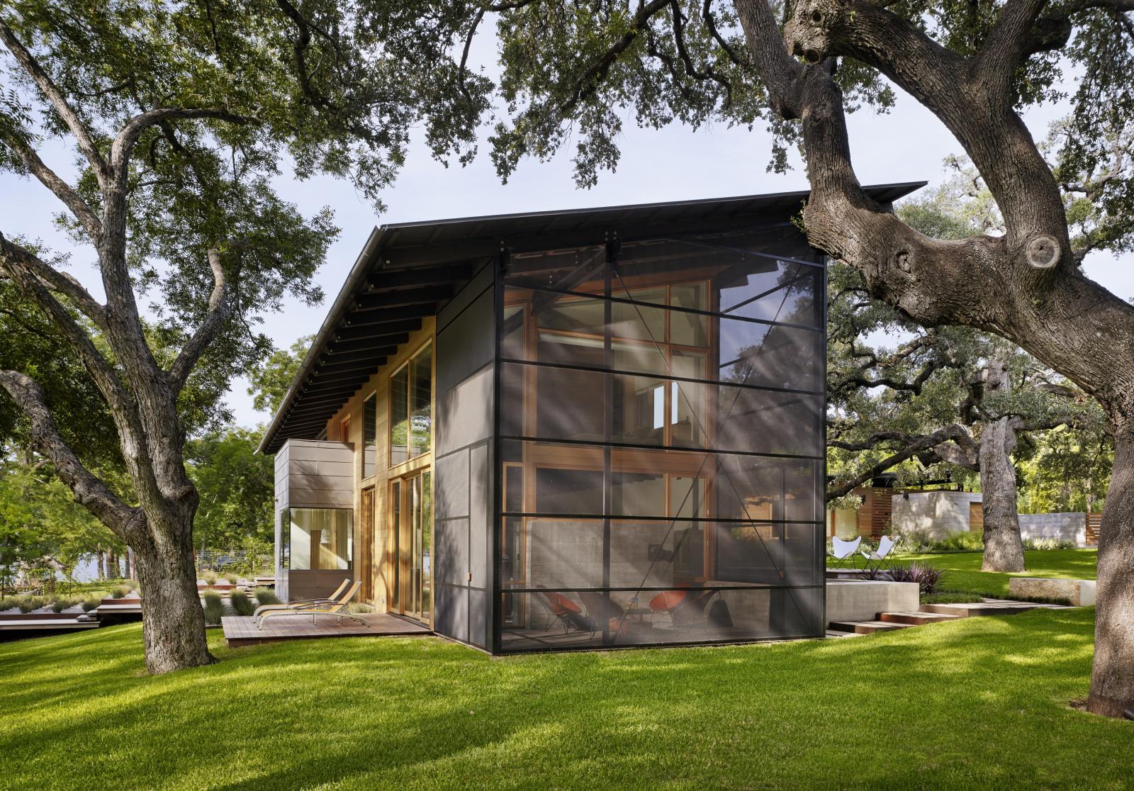 Hog Pen Creek Residence exterior view from screened in porch Situated at the confluence of Hog Pen Creek and Lake Austin, Hog Pen Creek Residence was envisioned by its owners as a place that evokes the playfulness of summer on the lake. Twin porches and a two-story living area, with a treetop level master bedroom l