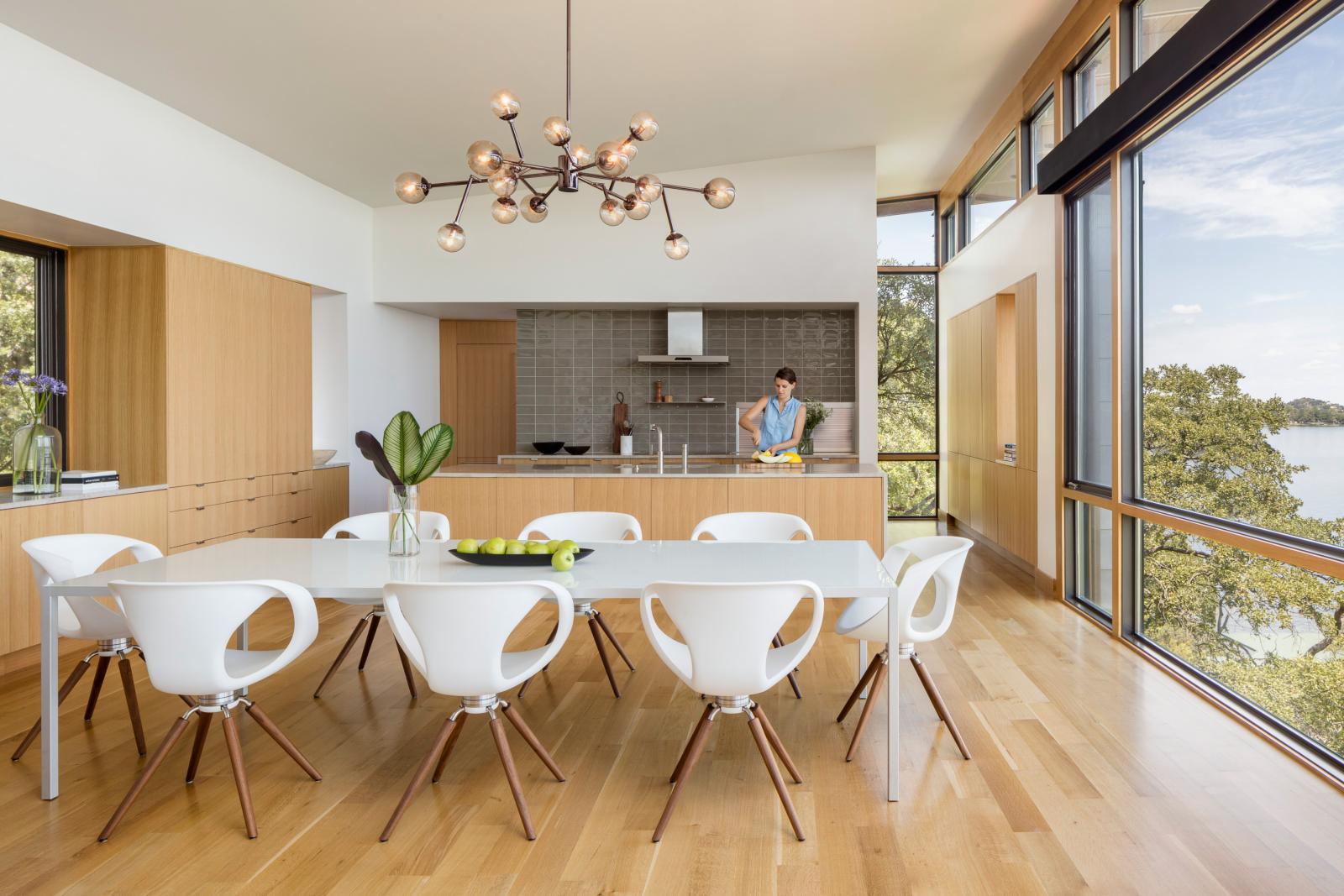 Looking through open concept living, dining, kitchen with views to outside. An award winning vertically structured lake house The long, narrow three-story residence dramatically culminates at the top floor, set just above the tree line and providing a nearly 180-degree view of the lake beyond